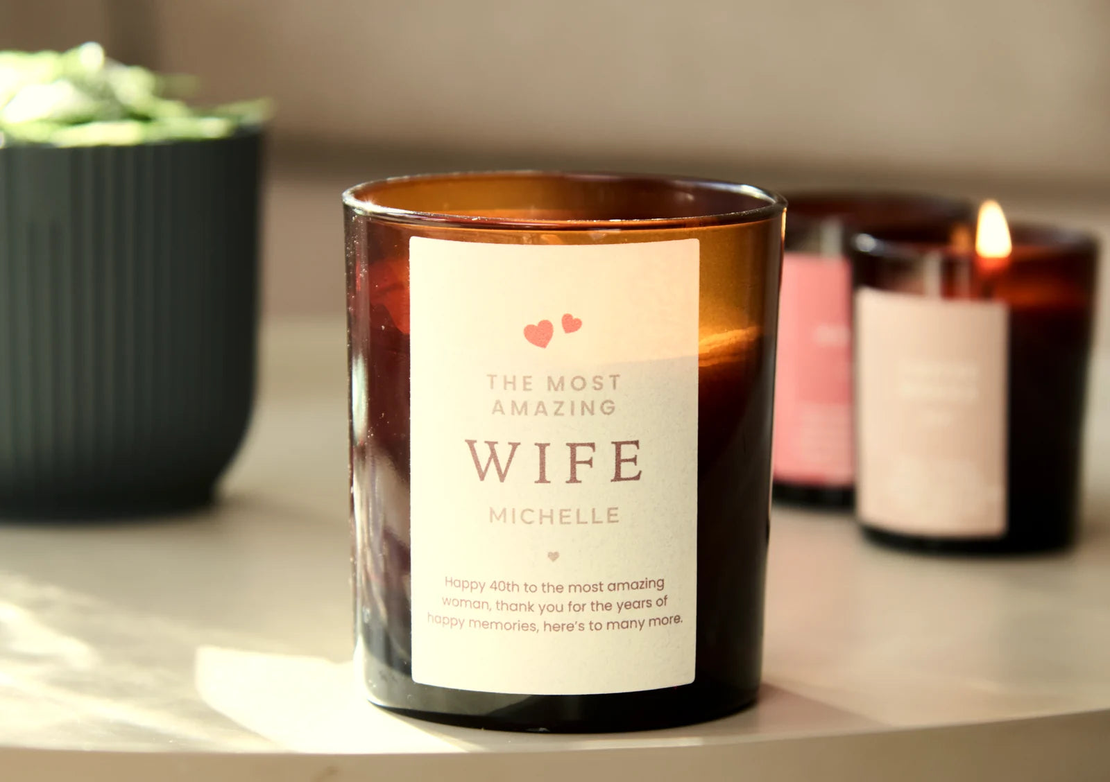 Amber glass candle with a personalised label reading The Most Amazing Wife, Michelle, and a happy 40th message, on a table with lit candles behind